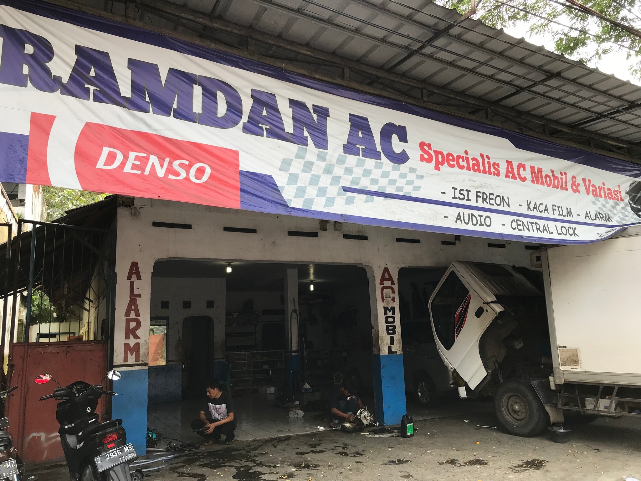 Foto area bengkel RamdanAC dengan teknisi sedang bekerja pada AC mobil